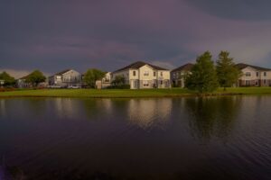 Lakefront homes reflecting on calm water under a dramatic cloudy sky