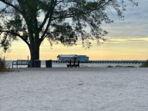 Beach at sunset with a wooden pier and a distant building along the shore