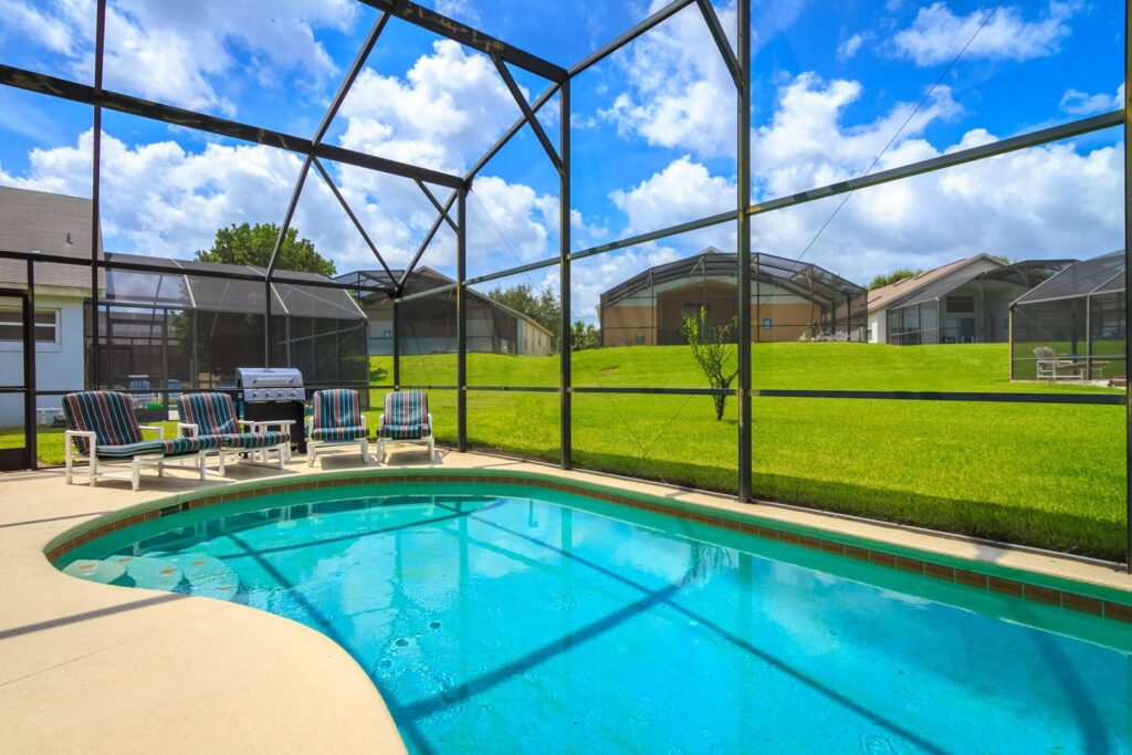 Enclosed backyard pool at a sunny Florida villa with lounge chairs and a grill