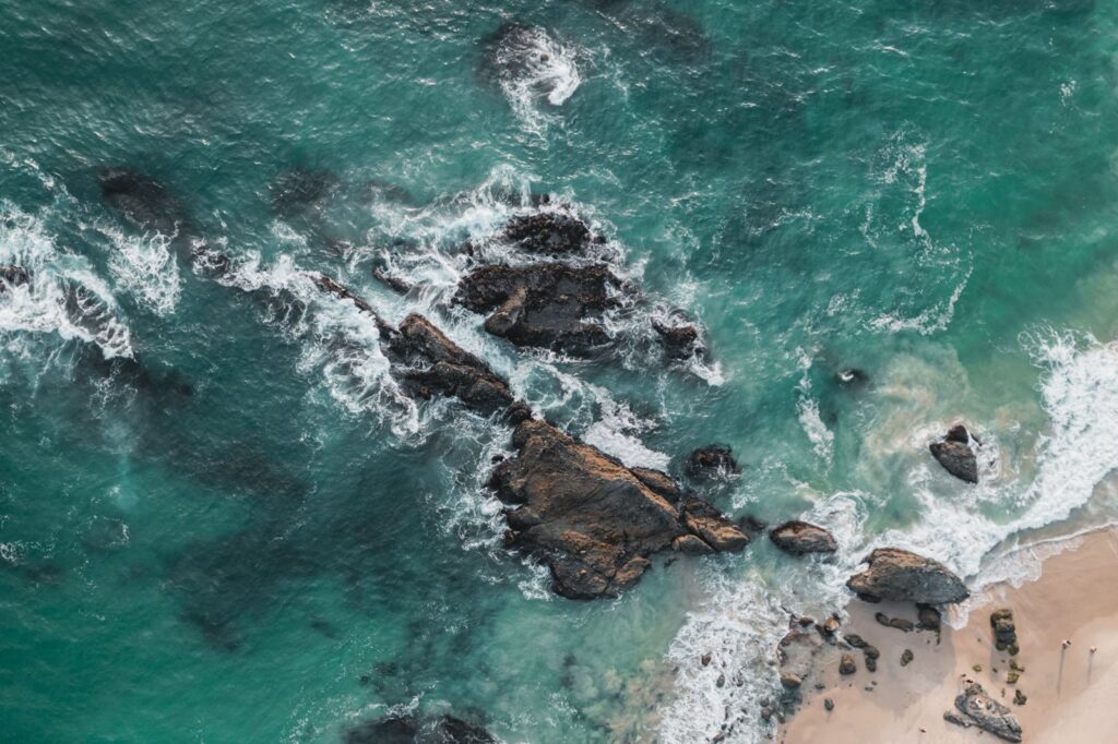 Aerial view of a rocky coastline with turquoise water and a sandy beach shore
