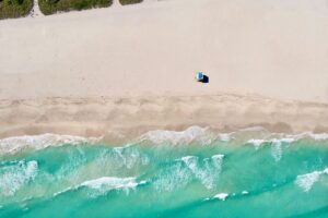 Aerial view of a wide sandy beach with a lifeguard stand, turquoise surf and dune grass