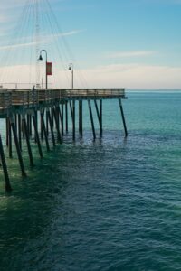 Wooden pier with lamps extending over blue ocean water under a pale sky