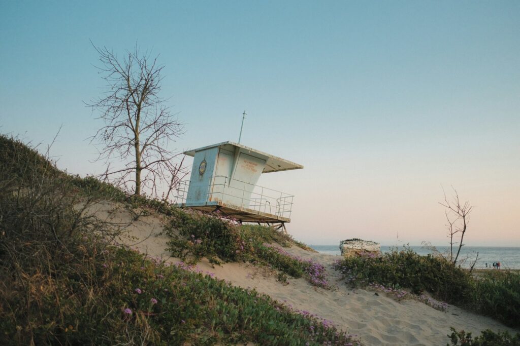 Beach with a lifeguard tower, sand dunes, and ocean waves under a clear sky.