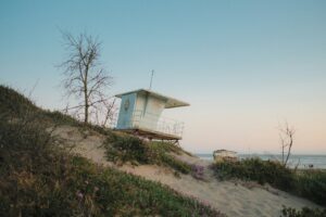 Beach with a lifeguard tower, sand dunes, and ocean waves under a clear sky.