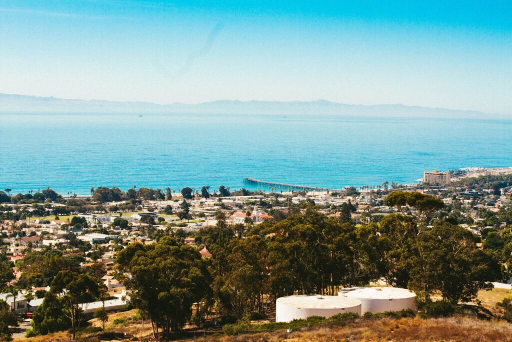 Aerial view of a coastal California town with buildings, ocean, and a long pier