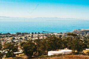 Aerial view of a coastal California town with buildings, ocean, and a long pier