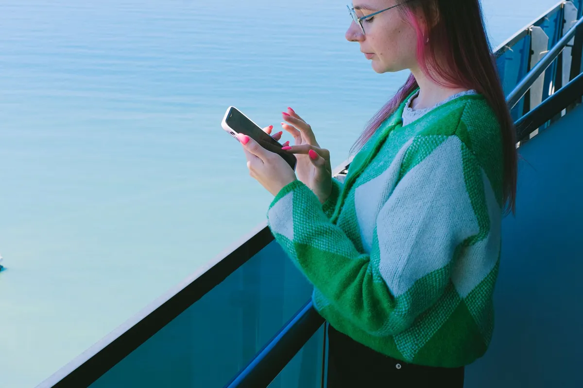 Woman using a smartphone on a balcony overlooking a calm ocean