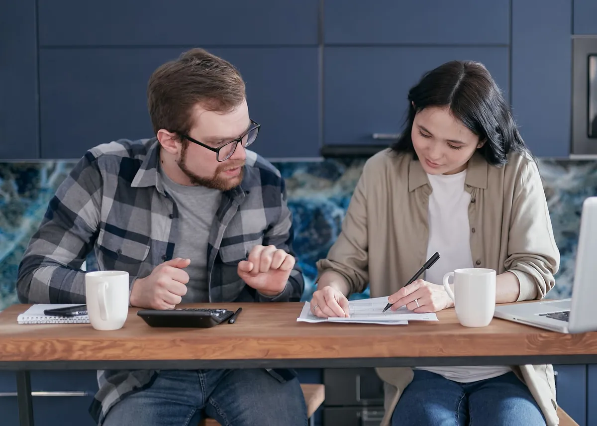 A couple sitting at a table with a laptop and calculator, reviewing finances together