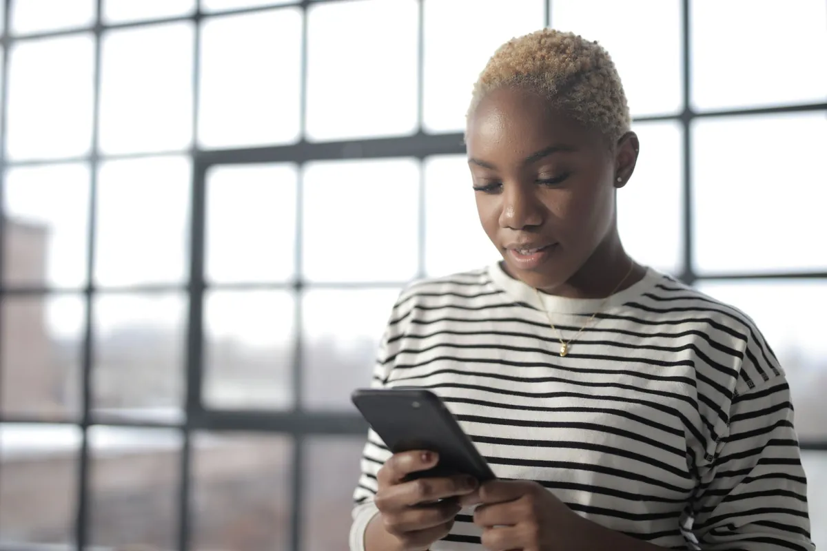 Young woman texting on her smartphone beside a window with natural light