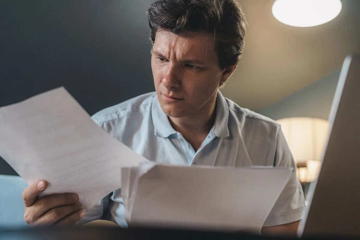 Man seated indoors reading papers under warm lighting