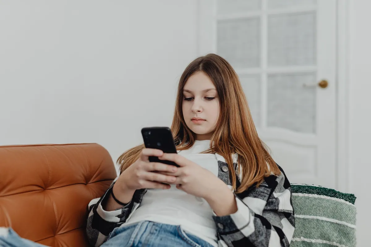 Teenage girl lounging on a sofa indoors while using her smartphone