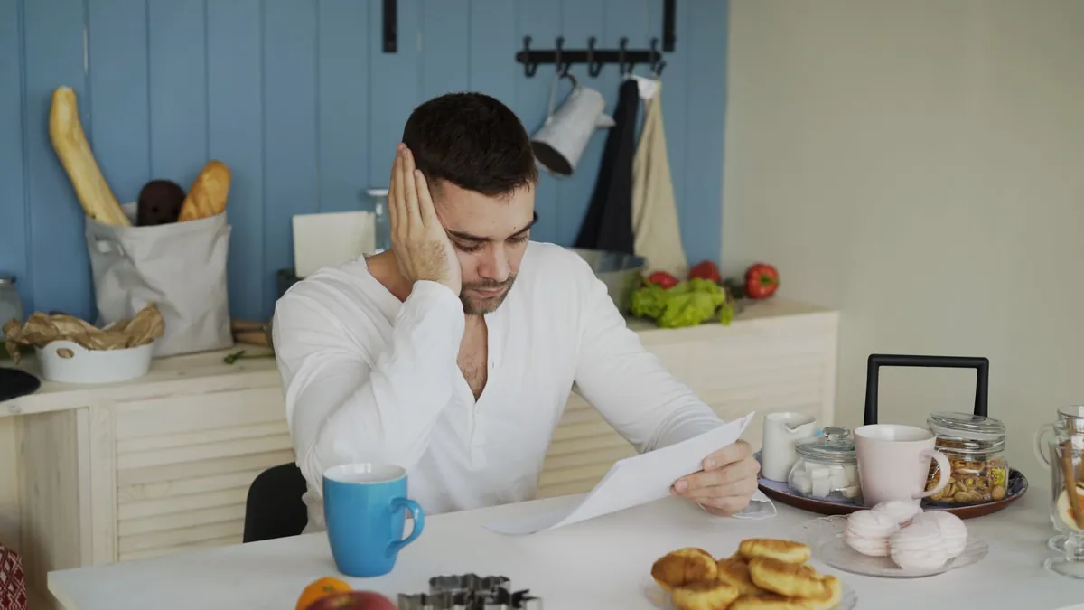 Man in white shirt reading a document at a kitchen table with breakfast