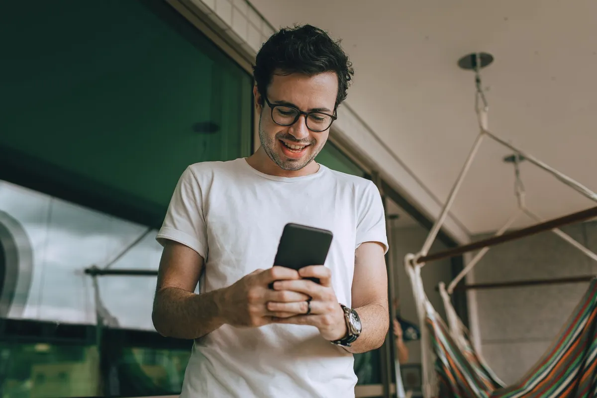 Young man with glasses checking his smartphone on a balcony