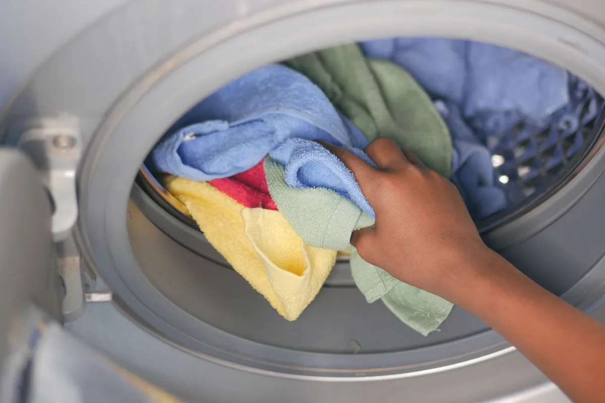 A hand placing colorful towels into a front-loading washing machine.